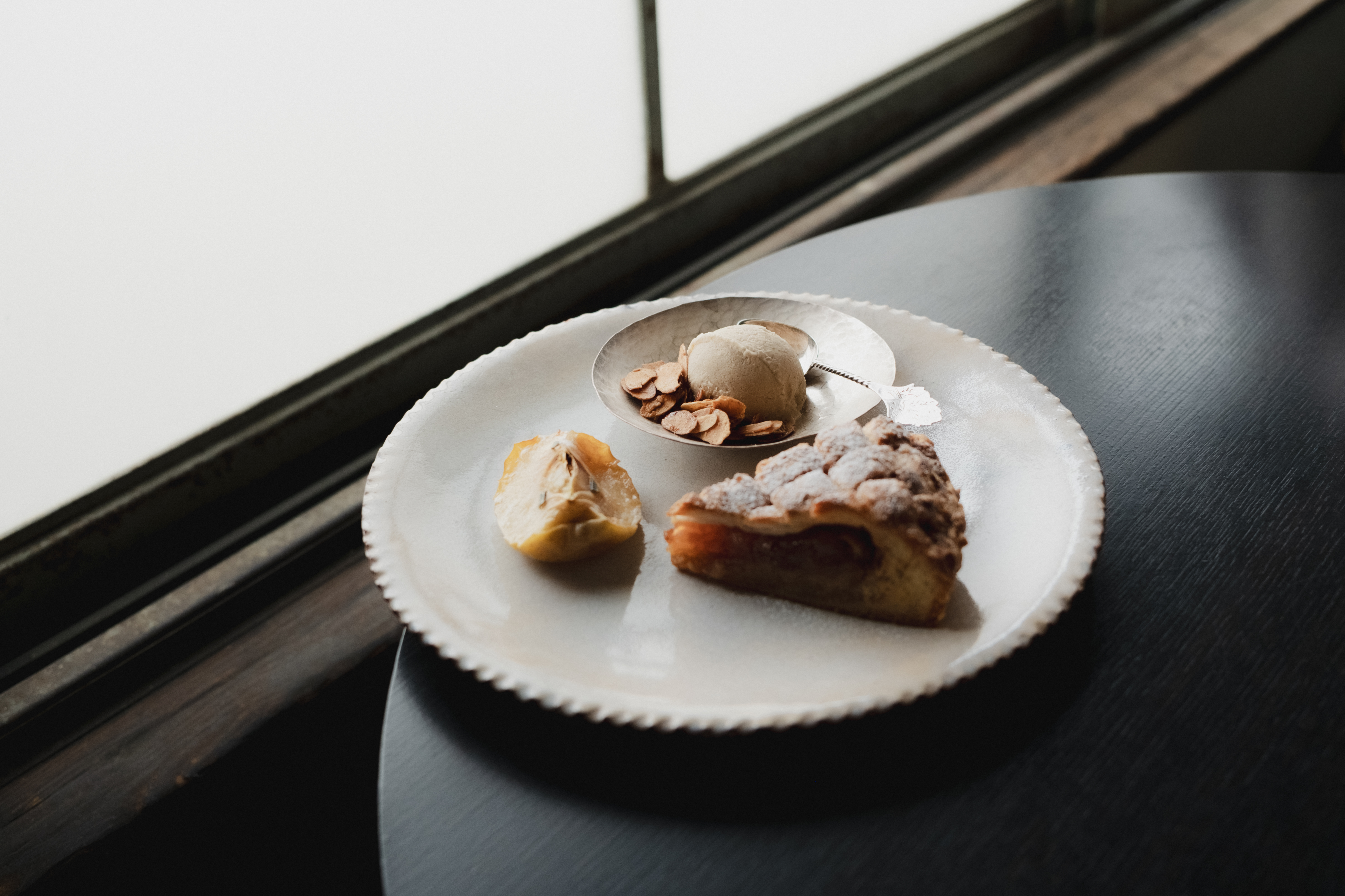 Apple pie with ice cream and sliced almonds on a white plate by the window